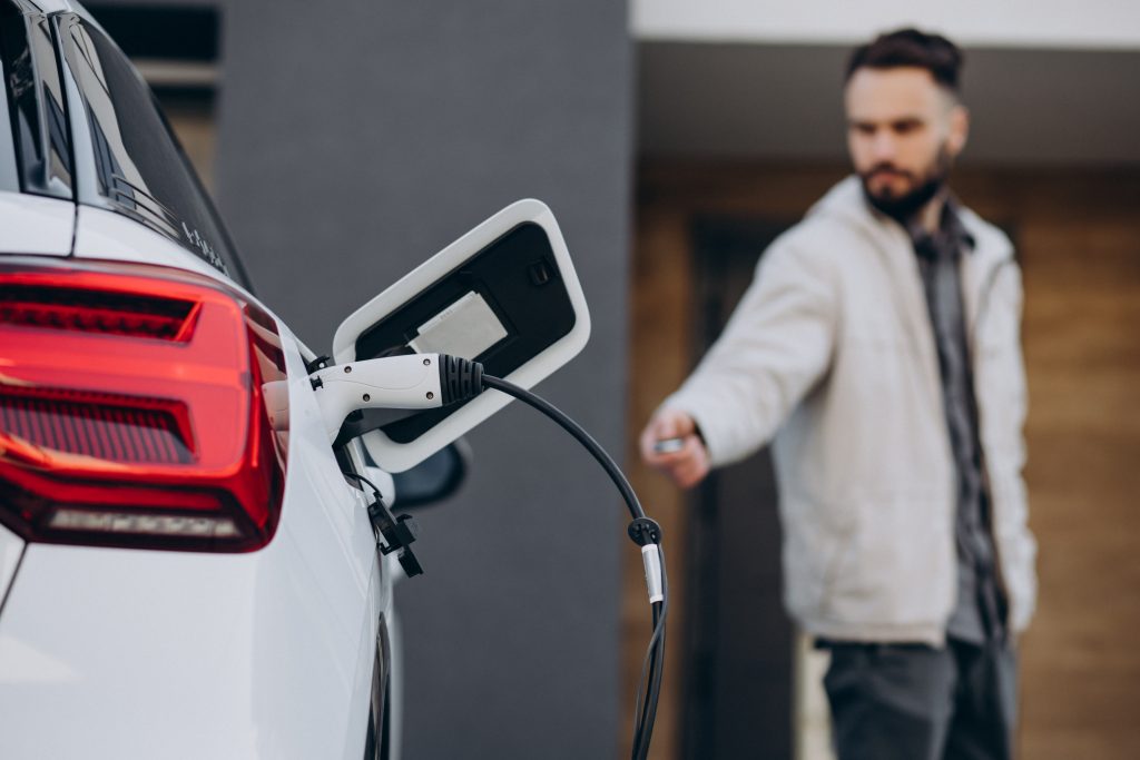 Man charging electric car by the house