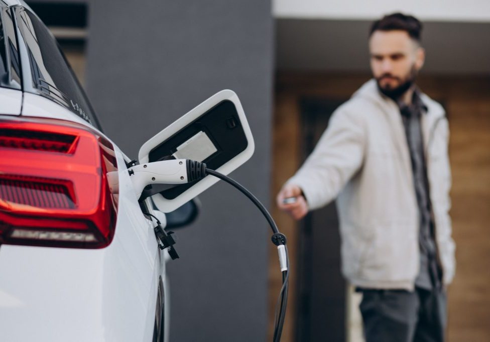 Man charging electric car by the house